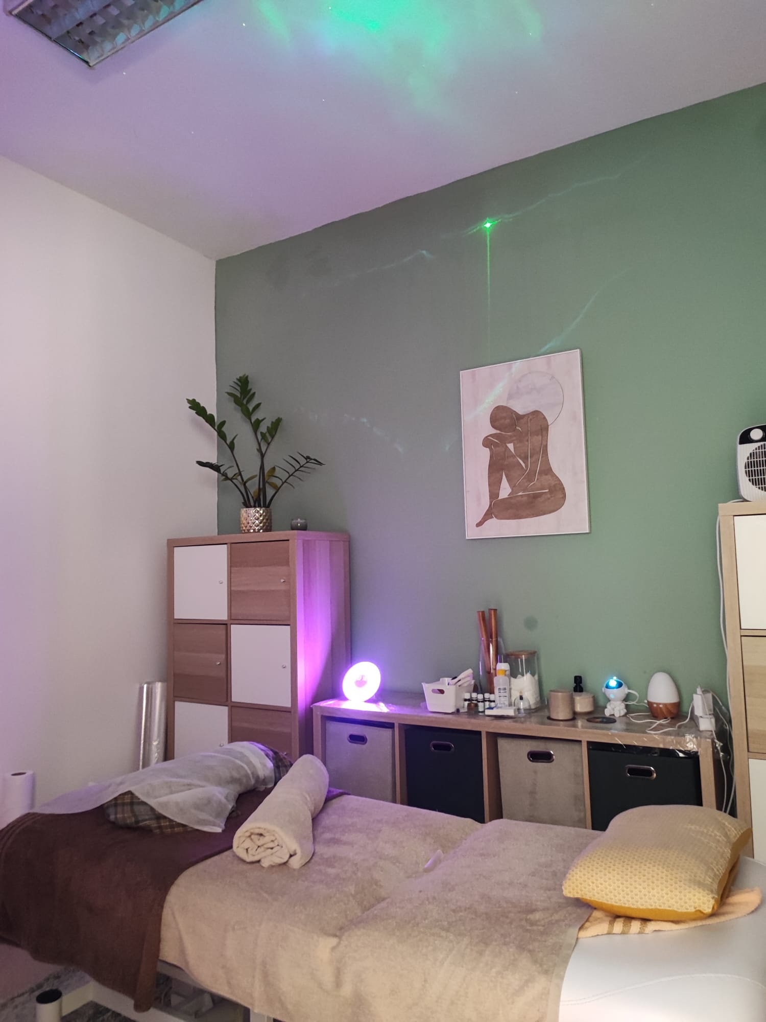 Sala de tratamento com marquesa, toalhas, parede verde e luz ambiente suave