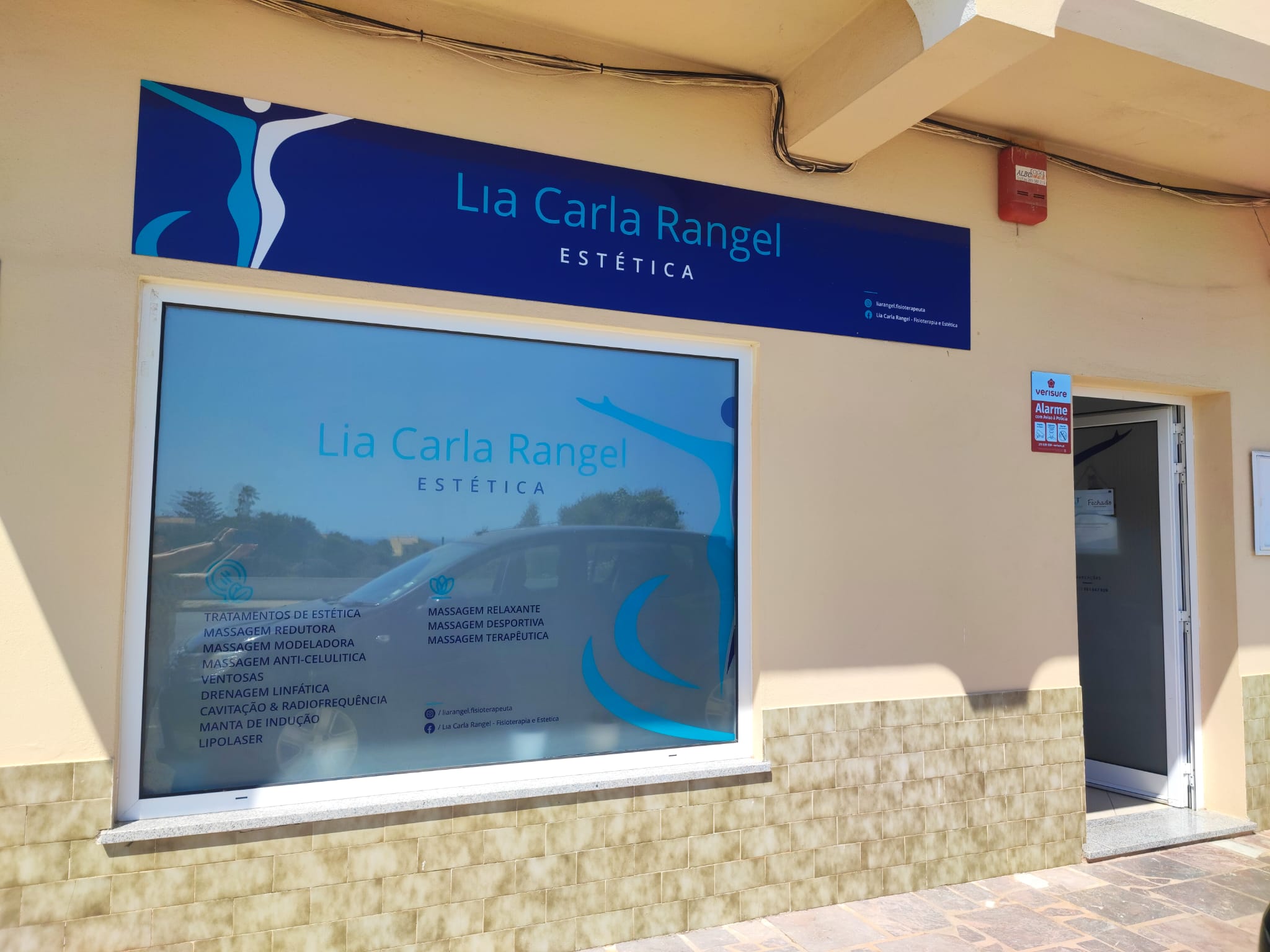 Fachada da clínica com a placa azul Lia Carla Rangel e a montra com a lista de tratamentos