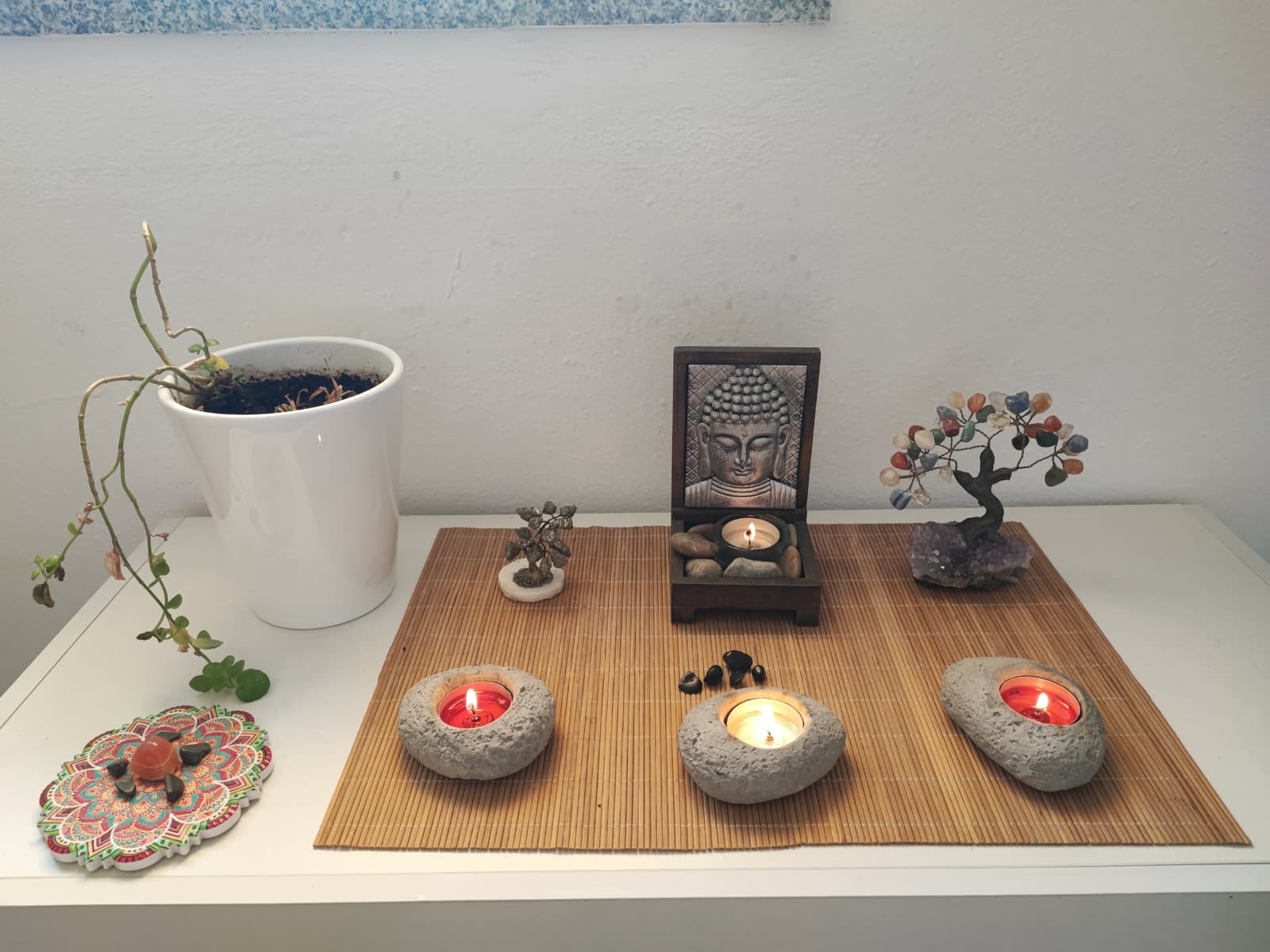 Cantinho zen: buda, velas em suportes de pedra e árvores de cristais sobre esteira de bambu