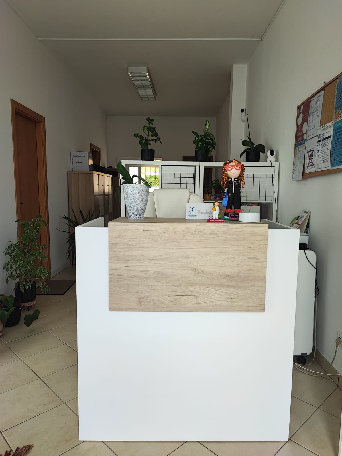 Receção da clínica: balcão branco e madeira, plantas e um corredor ao fundo
