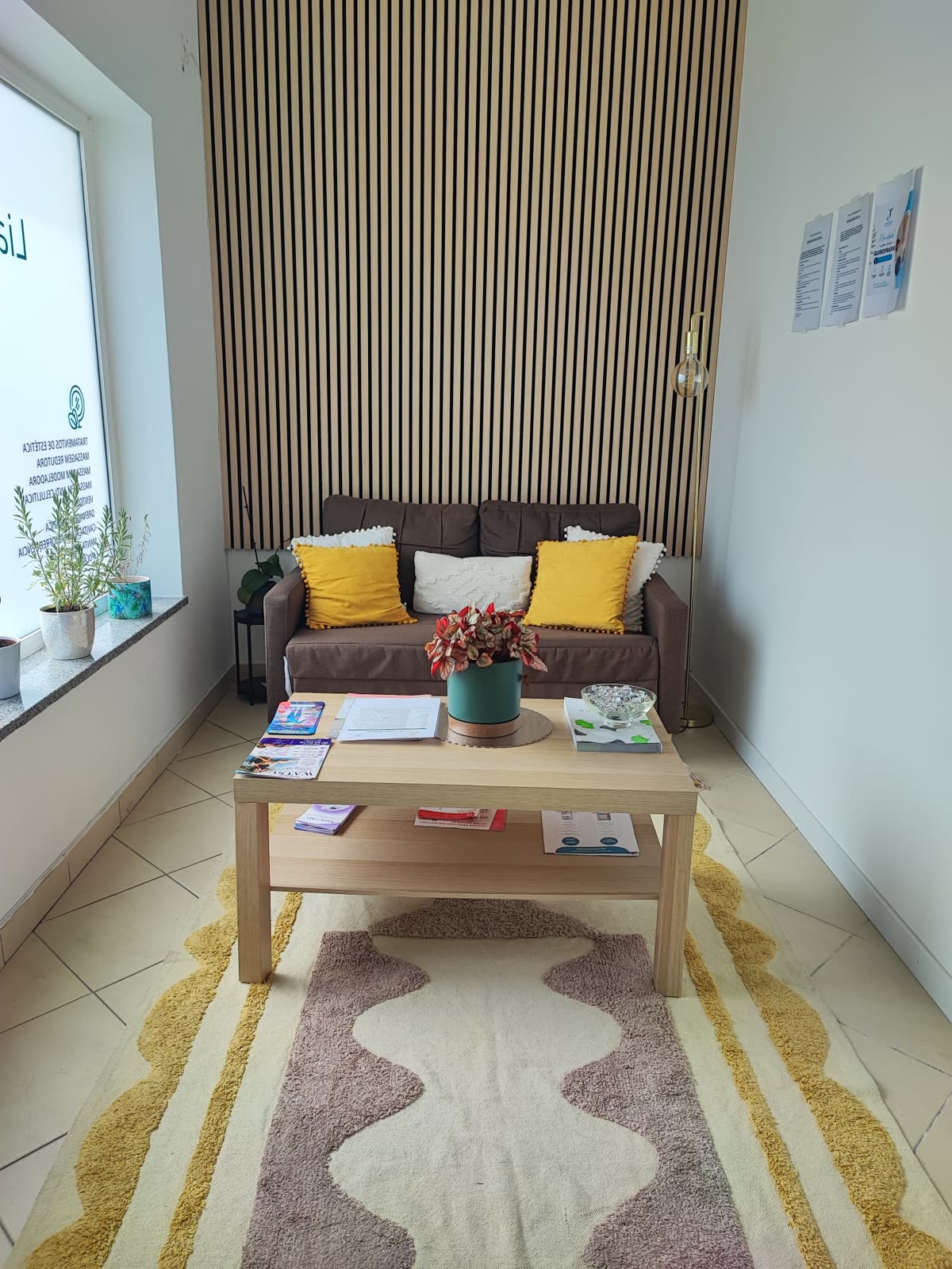 Sala de espera com sofá, almofadas amarelas, mesa de madeira e parede de ripas